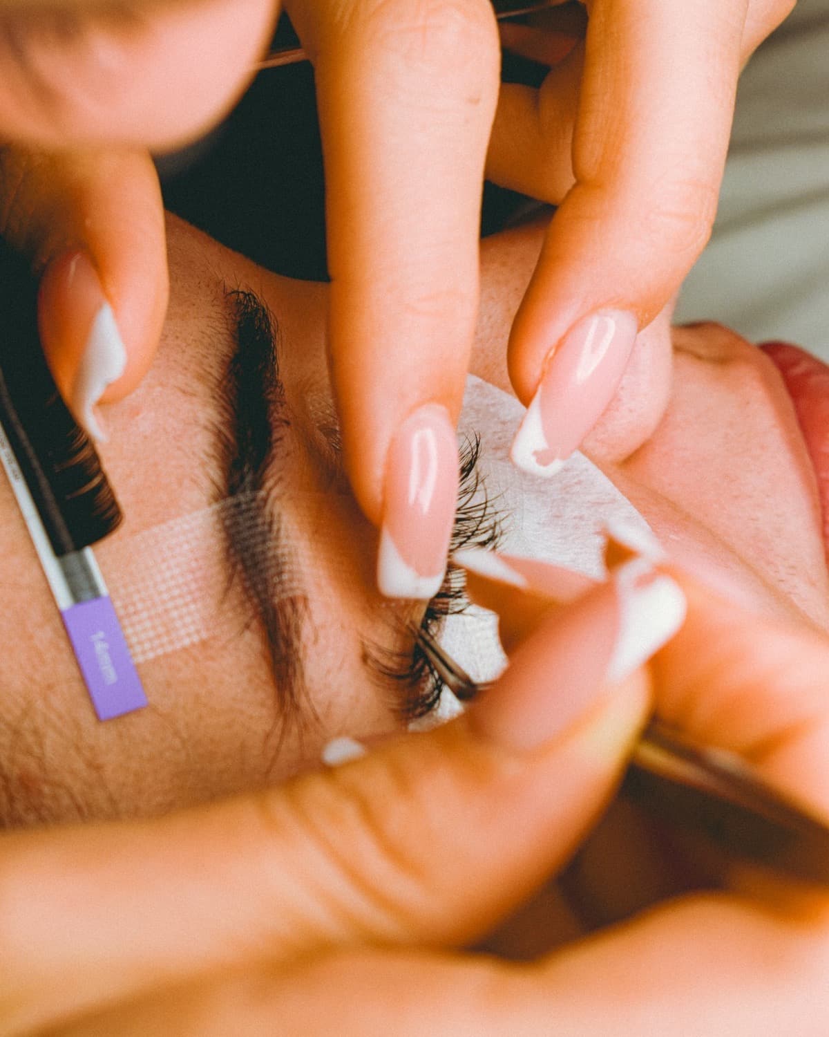 A beautician's hands working close to a client's lash line