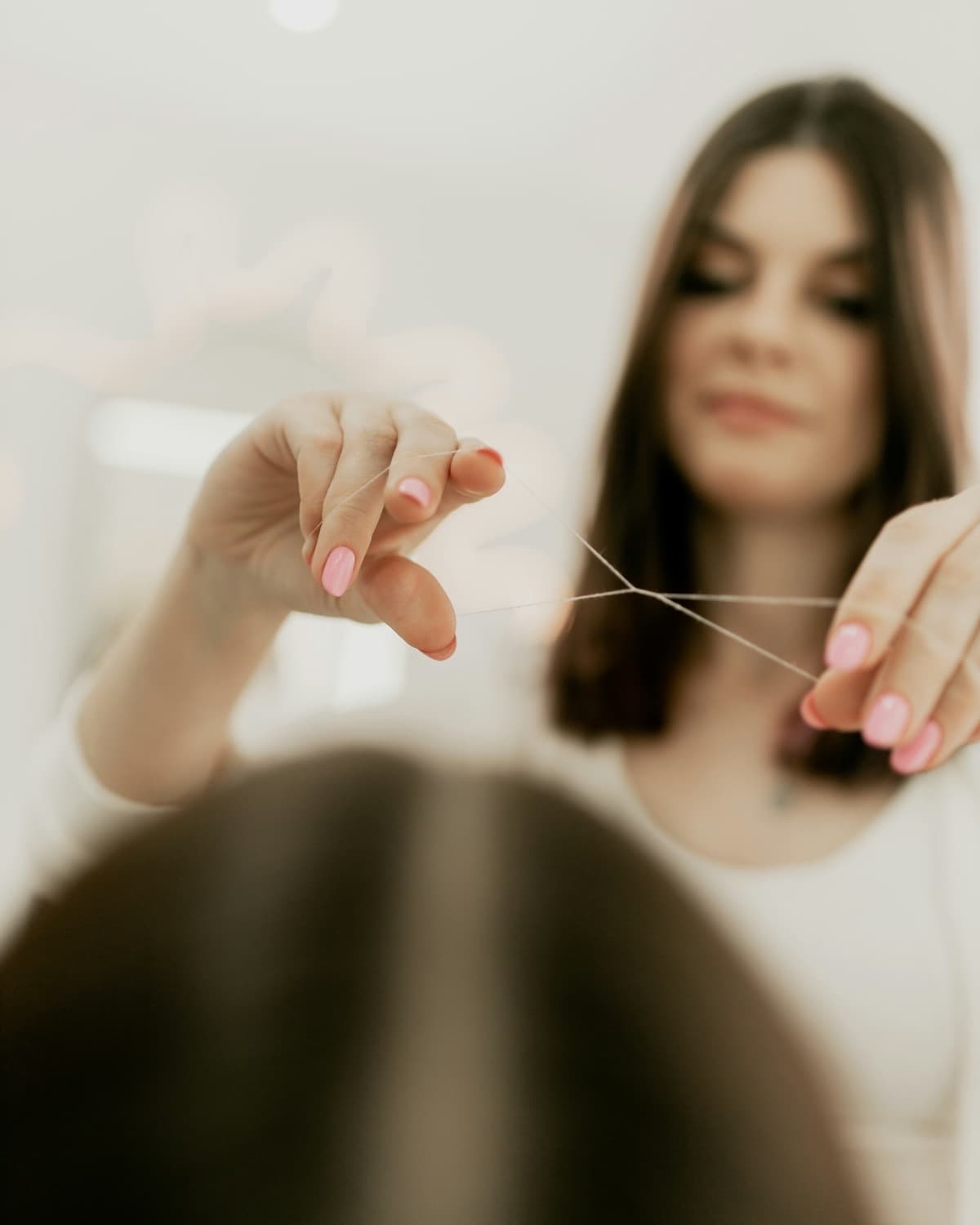 A beautician holding a loop of cotton thread, ready to shape a brow